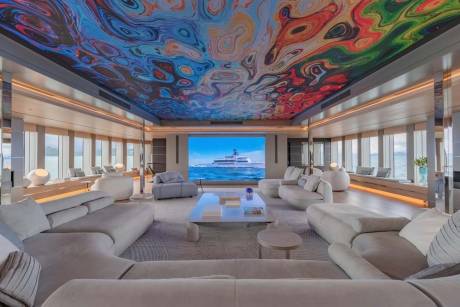 A luxurious yacht lounge boasts a vibrant, swirling ceiling mural and a large screen displaying a majestic vessel at sea.