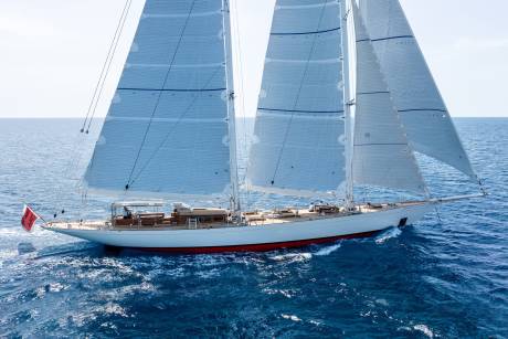 A majestic sailing yacht glides through the azure ocean under a clear sky, its sails billowing in the wind.