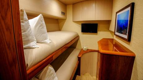 Luxurious bunk beds offer a cozy retreat aboard this elegant yacht, complete with a flat-screen TV and ocean-themed artwork.