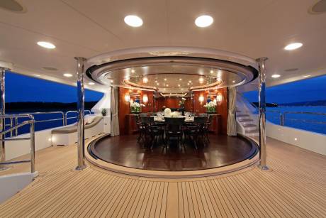 An elegant dining area on a yacht deck is illuminated by soft lights against the twilight sky.