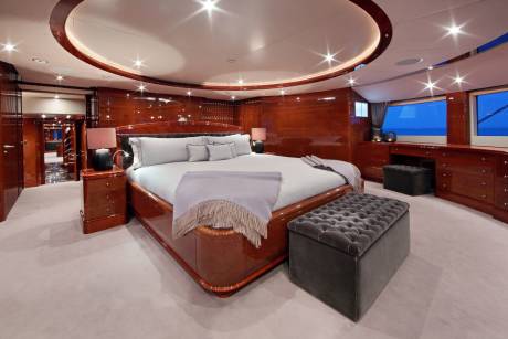 Luxurious yacht master suite features a king-sized bed, rich wood paneling, and panoramic ocean views.