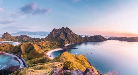 Golden hills meet turquoise waters under a pastel sky at this breathtaking Indonesian island vista.