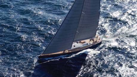 A sleek, black-sailed yacht glides across the deep blue waters, leaving a trail of white foam in its wake.