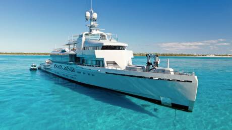 A luxurious superyacht glides through crystal-clear turquoise waters under a bright blue sky.