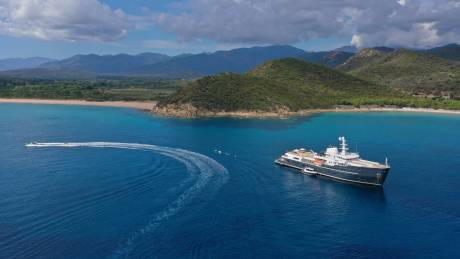 A luxurious yacht anchors in a pristine bay with lush green hills meeting the turquoise sea.