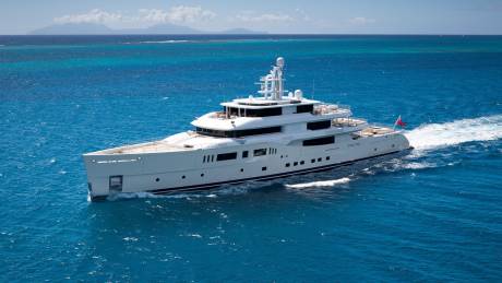 A luxurious white yacht cruises through the vibrant turquoise waters of the Caribbean under a clear blue sky.