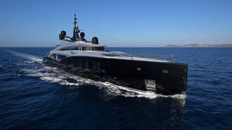A sleek black yacht glides through the deep blue ocean under a clear sky, leaving a foamy wake.