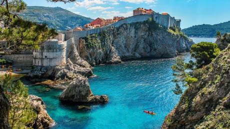 Kayakers paddle through the crystal-clear turquoise waters beneath the ancient stone walls of Dubrovnik, Croatia.