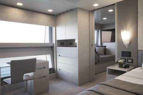 A modern and minimalist bedroom interior with built-in storage units, a cozy seating area, and a large window providing natural light.