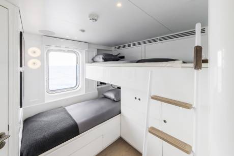 Bunk beds offer a cozy sleeping arrangement with a view of the ocean through a porthole window.