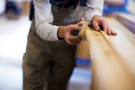 A craftsman meticulously sands a wooden surface, creating fine dust particles that catch the light.