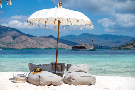 Relax on a pristine beach with comfortable seating and a traditional parasol overlooking a tranquil turquoise bay.