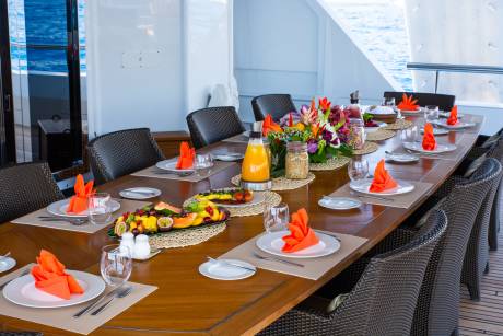A beautifully set table awaits a delightful breakfast on a yacht deck overlooking the sparkling blue ocean.