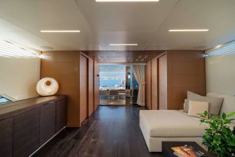 A modern and minimalist interior design with a long hallway, wooden floors, and various furniture pieces, including a couch and a decorative plant.