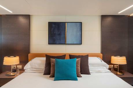 A modern and stylish bedroom with a large bed, plush pillows, and a framed artwork on the wall, complemented by warm lighting and a minimalist design.