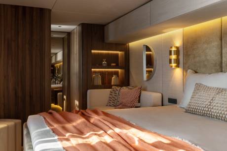 A luxurious bedroom features warm wood paneling, soft lighting, and a plush bed adorned with a coral throw.