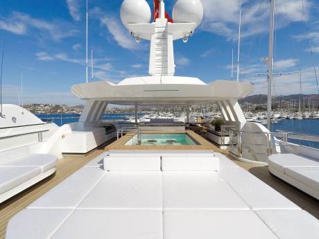 Relax in the onboard jacuzzi surrounded by plush white loungers and a picturesque marina view.