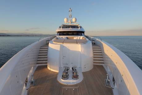 The sun casts a warm glow on the pristine deck of a luxurious yacht as it glides across the calm, blue sea.