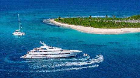 A luxurious yacht and a catamaran cruise the crystal-clear waters surrounding a lush tropical island.