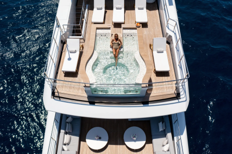 A woman relaxes in a luxurious yacht jacuzzi surrounded by sun loungers on a clear blue day.