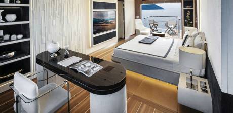 Luxurious yacht cabin offers a sleek workspace and a comfortable bed with a stunning ocean view.