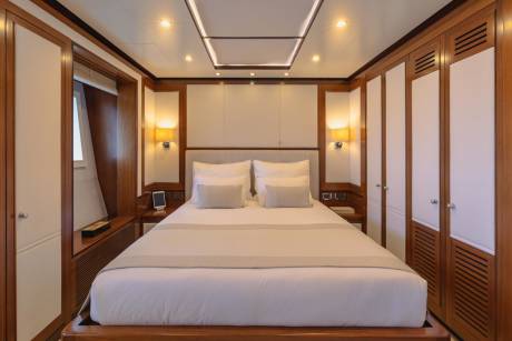 Luxurious yacht cabin features a plush king-sized bed, warm wood accents, and ample closet space.