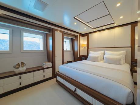Luxurious yacht cabin features a spacious bed, elegant wood accents, and stunning ocean views from the windows.