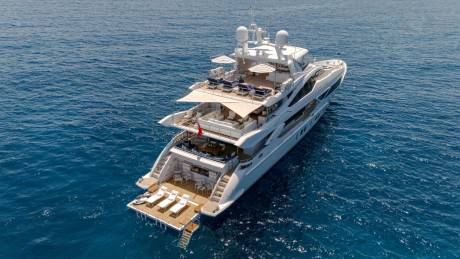 A luxurious white yacht with multiple decks and lounge areas glides across the deep blue sea.