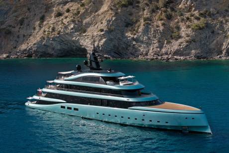 A sleek, modern yacht glides through the turquoise waters of a secluded bay, dwarfed by rugged, sun-drenched cliffs.