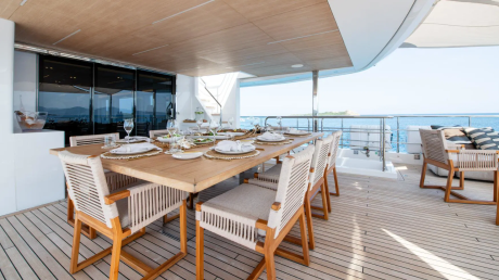 A beautifully set outdoor dining table awaits guests on a luxurious yacht deck overlooking the sparkling blue sea.