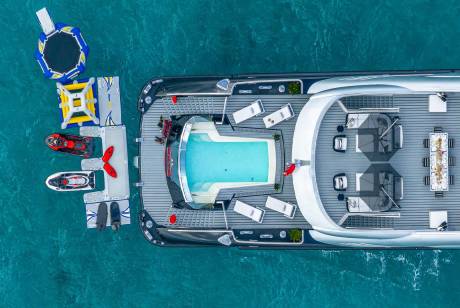 A luxurious yacht floats on turquoise waters, complete with a swimming pool, jet skis, and a dining area.