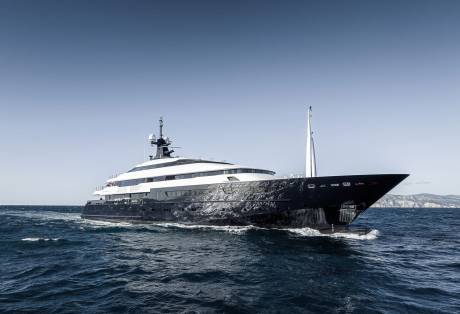 A sleek, dark yacht glides through the deep blue ocean under a clear sky.