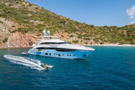 A sleek blue yacht anchors in a tranquil bay while a jet skier enjoys the turquoise waters under a clear blue sky.