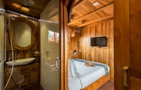 A luxurious wooden cabin features a sleek bathroom and a comfortable bed adorned with a straw hat.