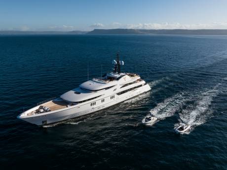 A majestic white superyacht cruises through the deep blue ocean, trailed by two smaller speedboats.