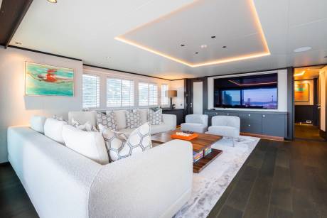 A luxurious yacht lounge features a plush white sofa, modern armchairs, and a large television displaying a scenic sunset.