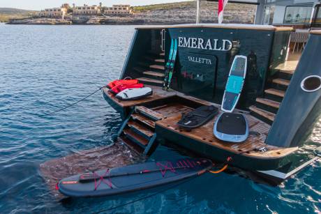 A collection of water sports equipment, including surfboards and jet skis, are neatly arranged on the deck of a luxury yacht.