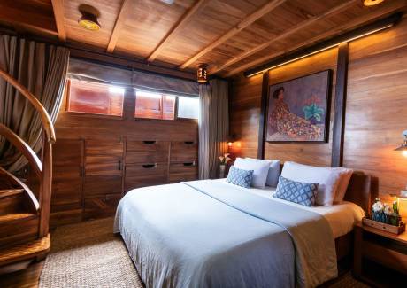 A cozy wooden cabin bedroom features a plush bed adorned with blue patterned pillows and a serene painting above the headboard.