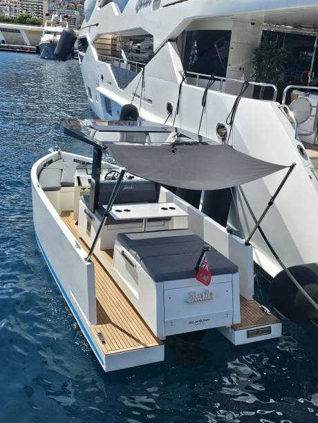 A sleek white tender boat with a grey canopy bobs gently in the blue water next to a large yacht.