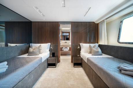 Twin beds flank a doorway leading to a modern ensuite bathroom, creating a serene sleeping space.