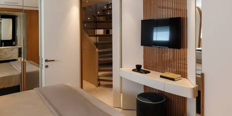 A modern bedroom features a sleek vanity, a television, and a view of a curved staircase.