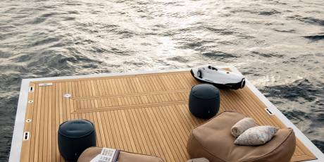 A sleek white watercraft rests on a teak deck beside comfortable seating overlooking the shimmering ocean.