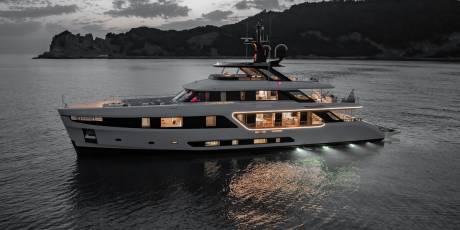 A luxurious yacht named Legend glides through calm waters at dusk, its interior lights casting a warm glow.