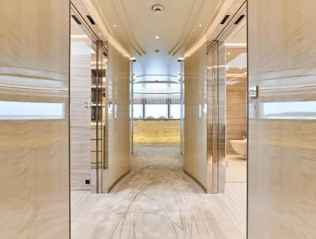 A luxurious, curved hallway with polished marble walls and a plush carpet leads to a brightly lit lounge area.