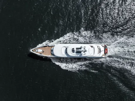 A sleek white yacht cuts through dark, rippling water, leaving a foamy white wake in its path.