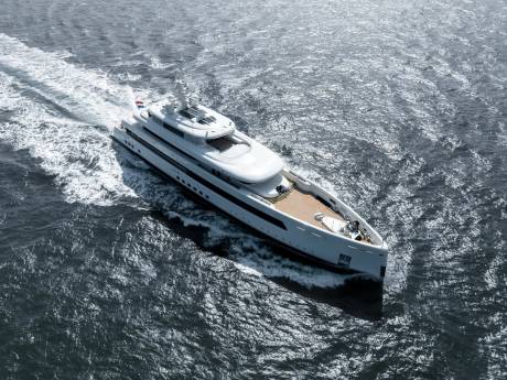 A sleek white superyacht glides through the choppy, sun-dappled ocean, leaving a foamy wake.