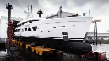 A magnificent white and black yacht rests on yellow cradles in a dry dock, awaiting its launch into the water.