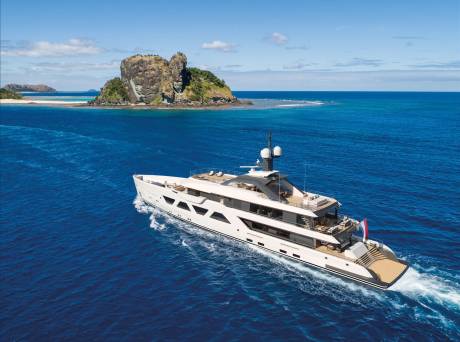 A luxurious white yacht cruises through the vibrant blue ocean near a rocky, verdant island.
