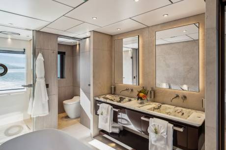 Luxurious yacht bathroom features a double vanity with marble sinks, a separate shower, and a toilet with a view of the water.