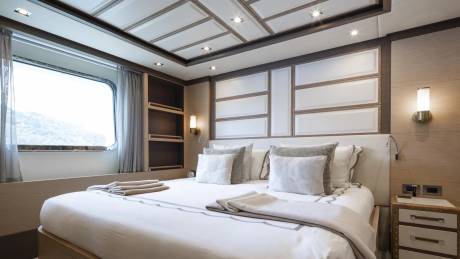 Luxurious yacht cabin features a plush bed, elegant wall paneling, and a large window with scenic views.